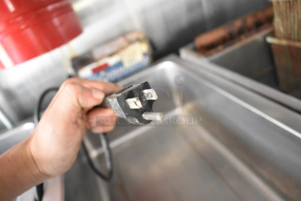 Hand holding a power plug inside a stainless steel food trailer kitchen.