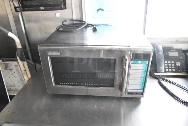 Sharp commercial microwave oven, model R-21J, stainless steel, 1000W, with keypad controls, on a stainless steel countertop.