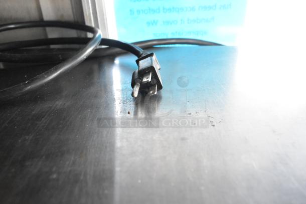 Power cord plug on a stainless steel countertop in a food trailer, indicating electrical readiness for kitchen appliances.