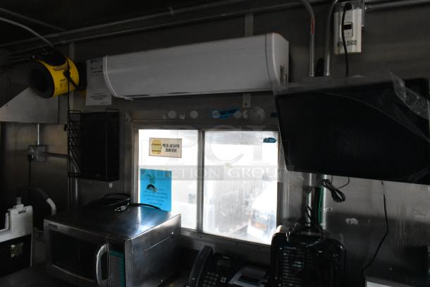 Interior of a fully equipped food trailer with commercial-grade appliances, including microwave and cooling systems. "Another Wing" sticker visible on window.