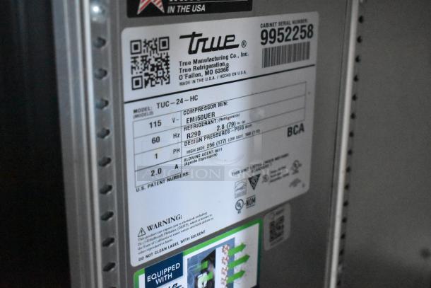 Close-up of True Refrigeration label on a mobile kitchen trailer. Model TUC-24-HC, serial 9952258. Contains compressor, refrigerant, and pressure details.