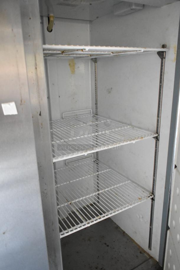 Inside view of a commercial-grade Arctic Air cooler with three white wire shelves, in used condition, for a food trailer setup.