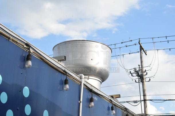 Blue food trailer exterior with industrial fan vent on top, surrounded by string lights under a partly cloudy sky.