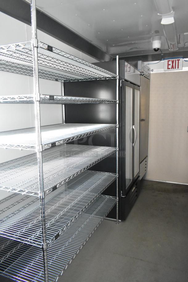 Fully equipped unbranded food trailer interior with metal shelving and commercial-grade refrigerator. Ready for operation.