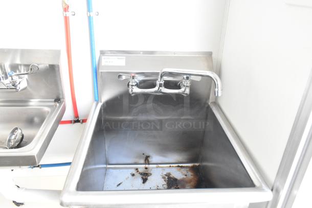 Stainless steel sink in a food trailer, featuring dual faucets and plumbing. Mild wear on the basin floor.