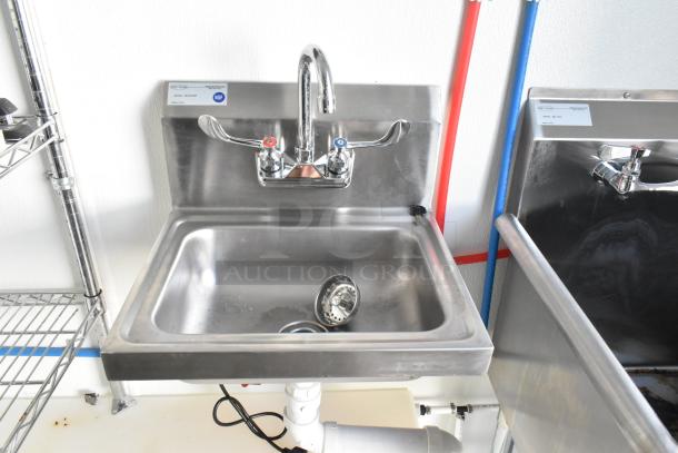 Stainless steel sink with NSF label in food trailer kitchen setup, featuring hot and cold faucets, and adjacent wire shelving.