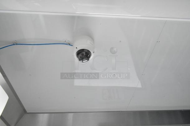 Security camera installed on ceiling of unbranded food trailer, visible blue cable, clean interior, new condition.