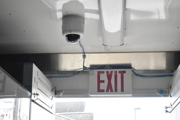 Ceiling of food trailer with dome security camera, fluorescent light, and red "EXIT" sign. Blue wiring visible.