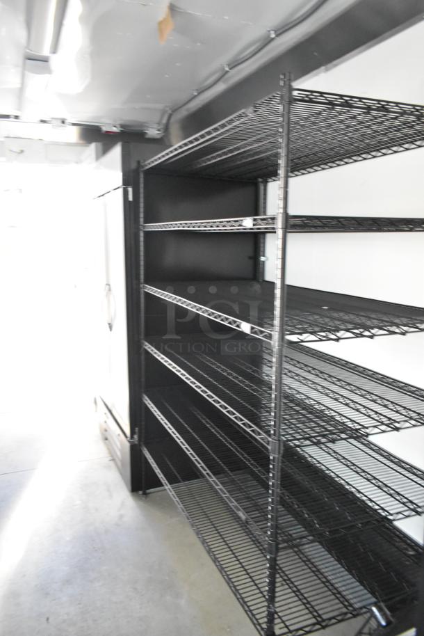 Black wire shelves and a large commercial refrigerator inside a brand new unbranded food trailer.