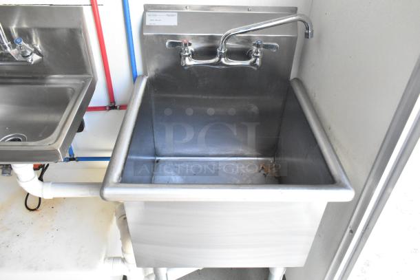Stainless steel sinks in a newly outfitted food trailer kitchen, featuring a large utility sink with attached taps and visible plumbing.