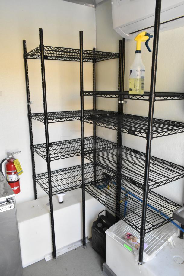 Black metal shelving unit inside a food trailer. Includes a Gage-Air cooler, fire extinguisher, and cleaning spray bottle.