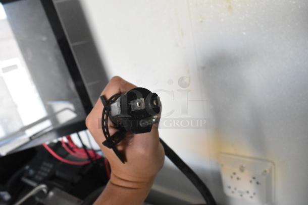 Close-up of a hand holding a black electrical plug within a new, fully equipped mobile kitchen trailer.