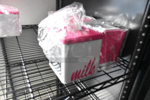 Plastic-wrapped pink and white containers labeled "milk" on a metal shelf, part of a food trailer setup.