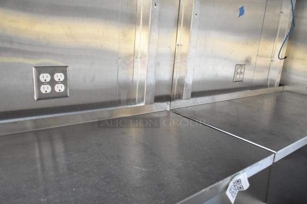 Unbranded food trailer interior with stainless steel counters, electrical outlets, and Coleman's Mack ventilation system.