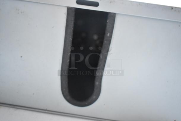 Close-up of a gray, angular metal surface with a narrow, dark recess, edges lined with black trim.