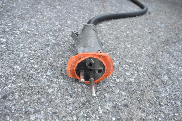 Power cable with an orange connector on asphalt. Details like possible brand or specific usage are not visible.