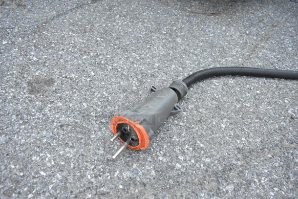 Close-up of a heavy-duty, three-pronged electrical plug with a thick black cable on asphalt.
