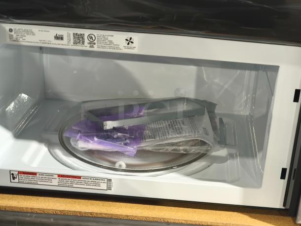 BRAND NEW SCRATCH AND DENT GE 1.7 cu ft Over-the-Range Sensor Microwave Oven, Model JVM6175SK6SS, interior view with manuals inside.