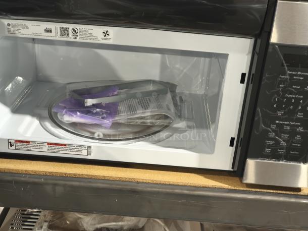 BRAND NEW GE 1.7 cu ft over-the-range microwave, model JVM6175SK6SS, sensor features, slight scratches. Tags indicate safety instructions.