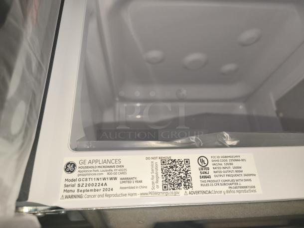 Brand new GE countertop microwave, model GCST11N1W1WW, 1.1 cu. ft. capacity. Scratch and dent condition. Tags show manufacture date September 2024, limited 1-year warranty, UL listed.