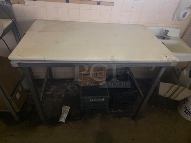 Stainless steel work table with cutting board, moderate wear. Features sturdy frame, ideal for kitchen prep.