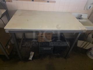 Stainless steel work table with cutting board, moderate wear. Features sturdy frame, ideal for kitchen prep.