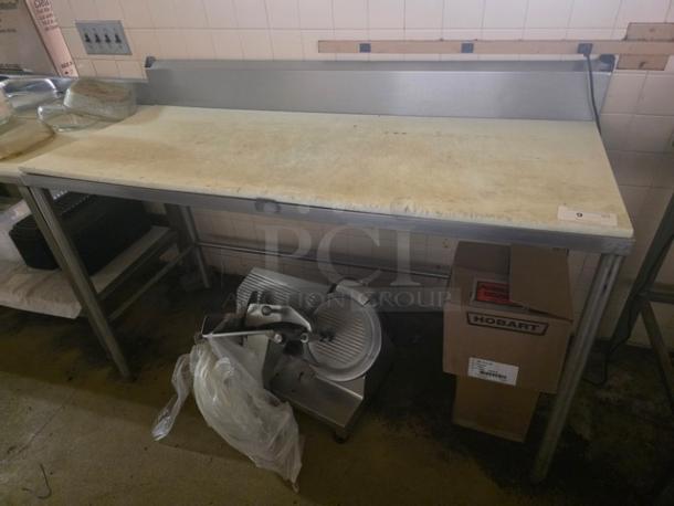 Stainless steel work table with cutting board, used condition, includes backsplash and bottom shelf. Features durable construction.
