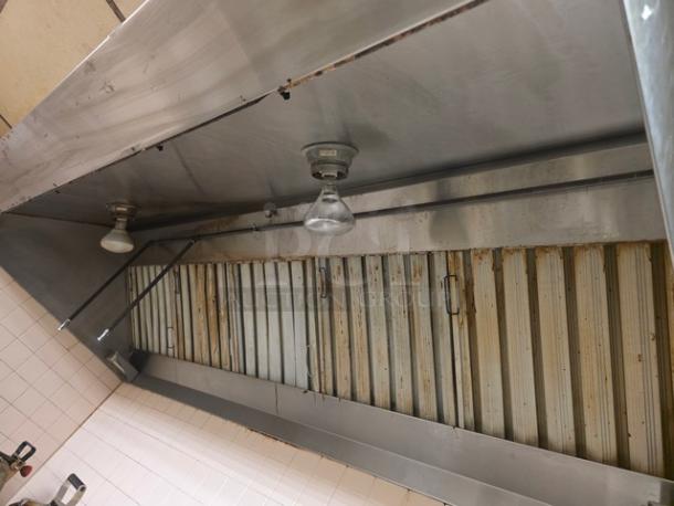 Commercial exhaust hood with stainless steel finish, overhead lighting, and multiple filters. Shows signs of wear.