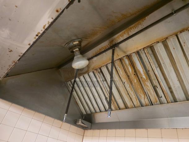 Commercial exhaust hood with stainless steel finish, visible grease residue, and integrated light fixture. Suitable for kitchen use.