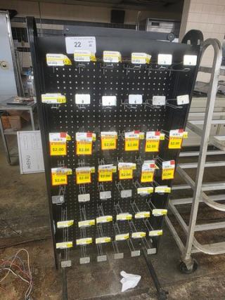 Black metal display rack with multiple hooks, labeled with price tags indicating $2.00 items. Used condition, pegboard design.
