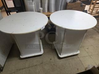Lot of 2 round white pedestal tables with some surface wear. Rectangular bases provide sturdy support. Suitable for home or office use.