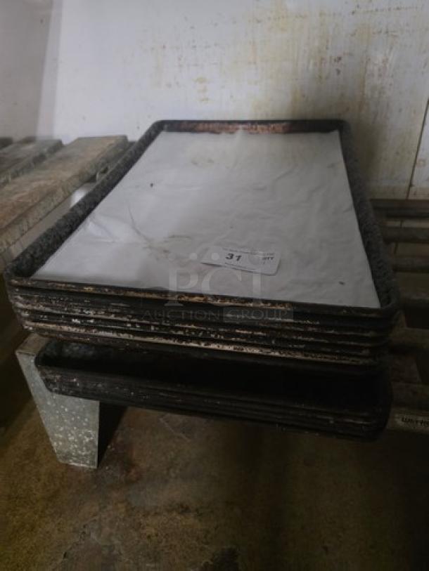 Lot of 13 full-size sheet pans in used condition, showing some wear. Pans are stacked, with clean paper covering.