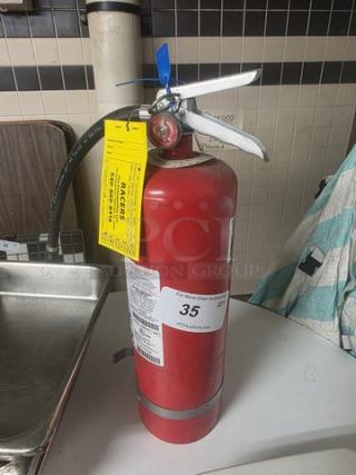 Red fire extinguisher with metal handle, yellow inspection tag, and gauge. Appears in good condition.