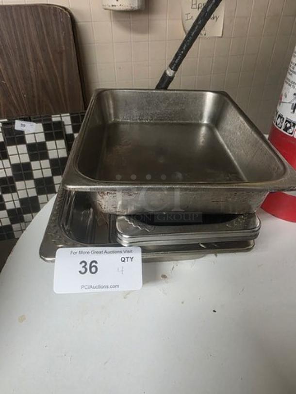 Lot of 4 stainless steel food pans, varying sizes. Some surface wear visible, ideal for catering or kitchen use.