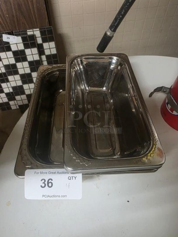 Lot of 4 stainless steel food pans, used, rectangular shape, stackable, reflective finish, shown with auction label.