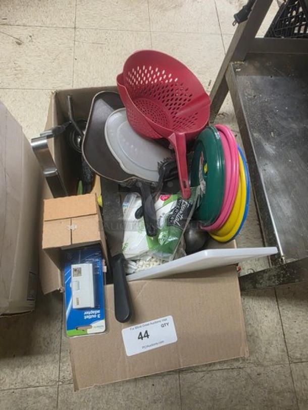 Lot of miscellaneous kitchenware including frying pans, a red colander, knives, plastic dishes, and a paper towel roll.
