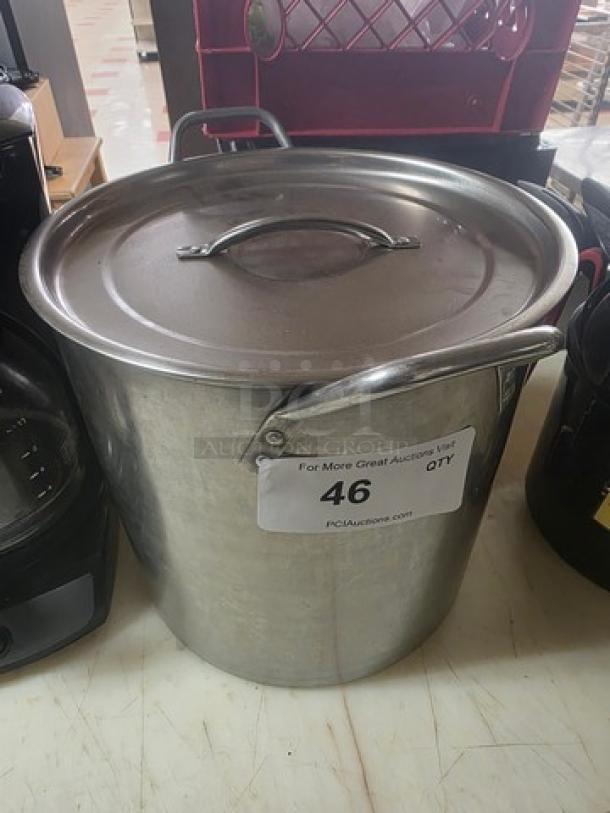 Large stainless steel stock pot with lid, featuring handles on sides. Visible auction label reads "46." Appears in good condition.