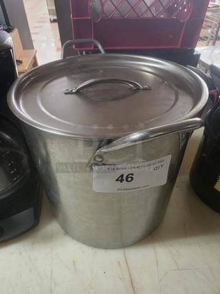 Large stainless steel stock pot with lid, featuring handles on sides. Visible auction label reads "46." Appears in good condition.