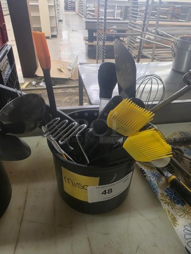 Lot of miscellaneous kitchenware in a black bucket, including spatulas, whisks, and brushes. Tag reads "misc," lot number 48.