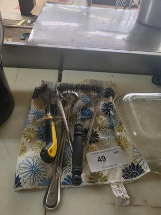 Lot of miscellaneous kitchenware including tongs, bottle opener, whisk, and ladle on floral cloth, labeled "49".