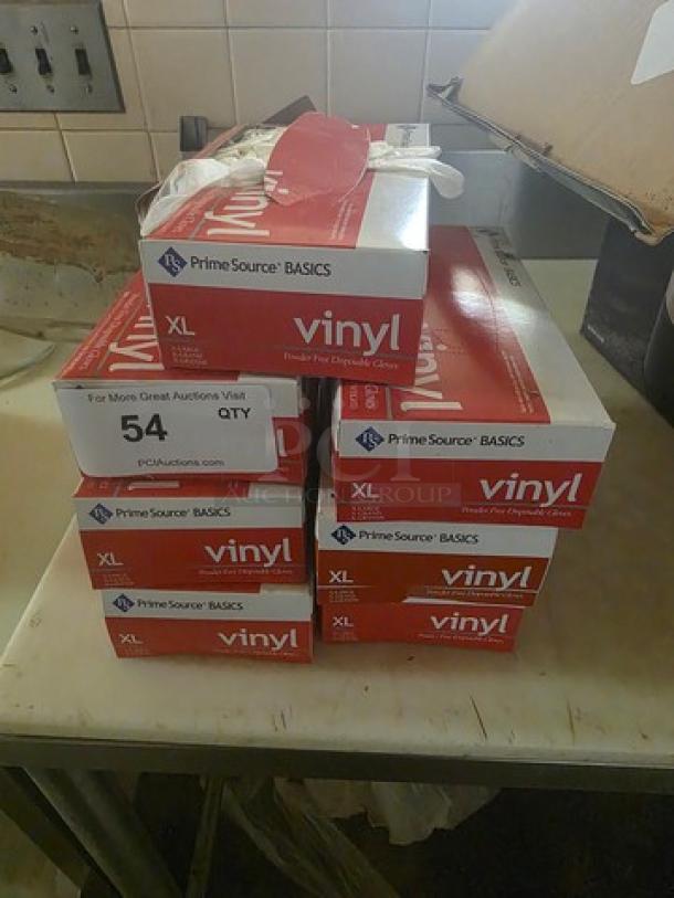 One lot of Fleetwood Model 1412 disposable gloves, size XL, in red "Prime Source" boxes, stacked on a table.