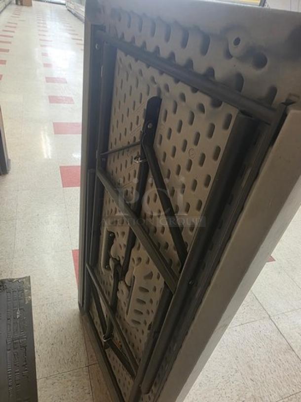 Foldable table with metal legs and sturdy plastic top, shown folded. Suitable for indoor or outdoor use. Good condition.