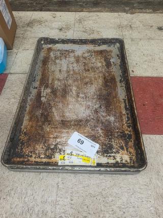 A stack of used sheet pans with visible wear, including scratches and rust. Auction label "69" attached.