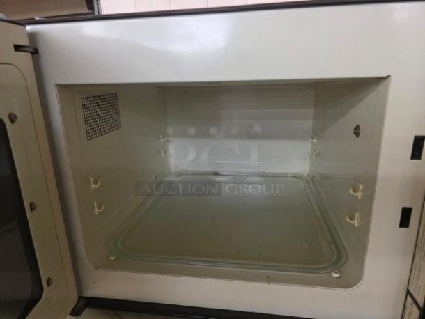 Vintage microwave interior, clean condition, features a glass turntable. No visible marks or labels. White and black trim.