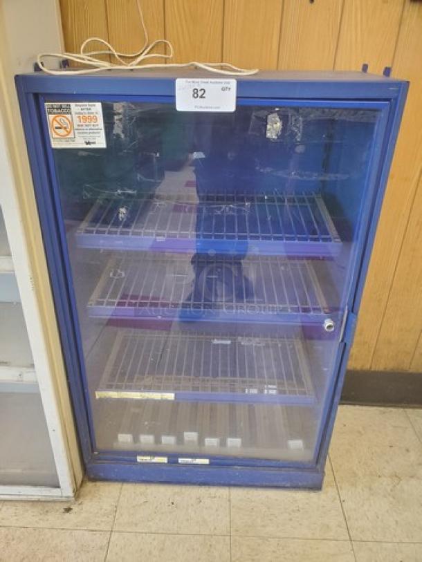 Blue, glass-door display case with three wire shelves. Minor wear visible on the glass and frame. Tag indicates auction lot 82.