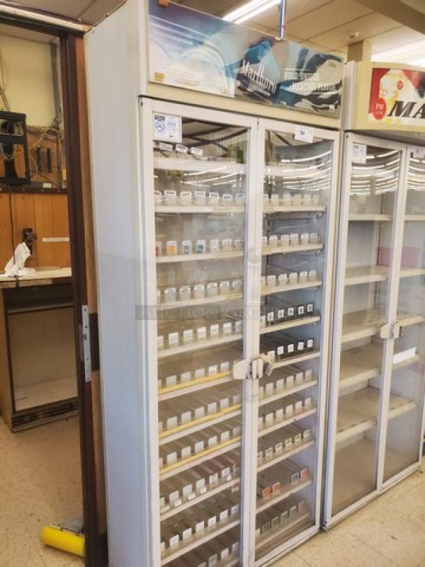 Freestanding cigarette display case with glass doors, multiple shelves stocked with cigarette packs. Used retail condition.