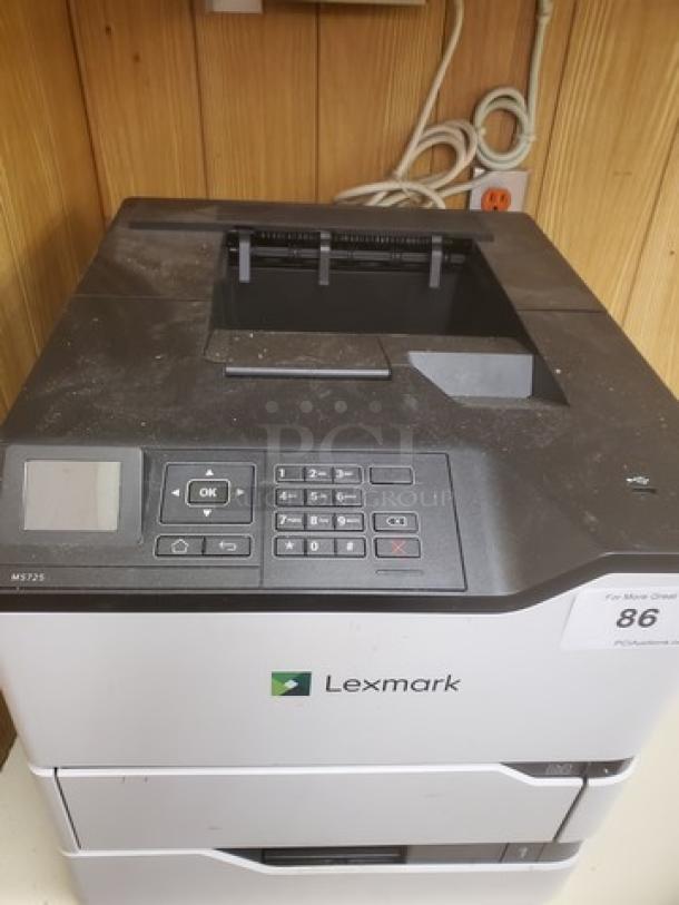 Lexmark MS725 monochrome laser printer, showing control panel and keypad. Mild surface dust, model label visible.
