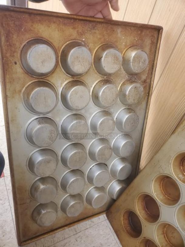 Lot of 2 muffin/cupcake baking pans, each with 24 cups. Used condition, visible wear and surface discoloration.