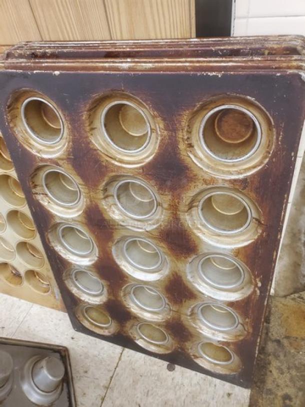 Lot of 8 well-used muffin/cupcake pans, each with 24 molds, showing signs of wear. Perfect for bulk baking.