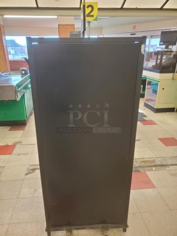 Tall black Checklane shelving unit in used condition, featuring four caster wheels. Located in a retail setting.